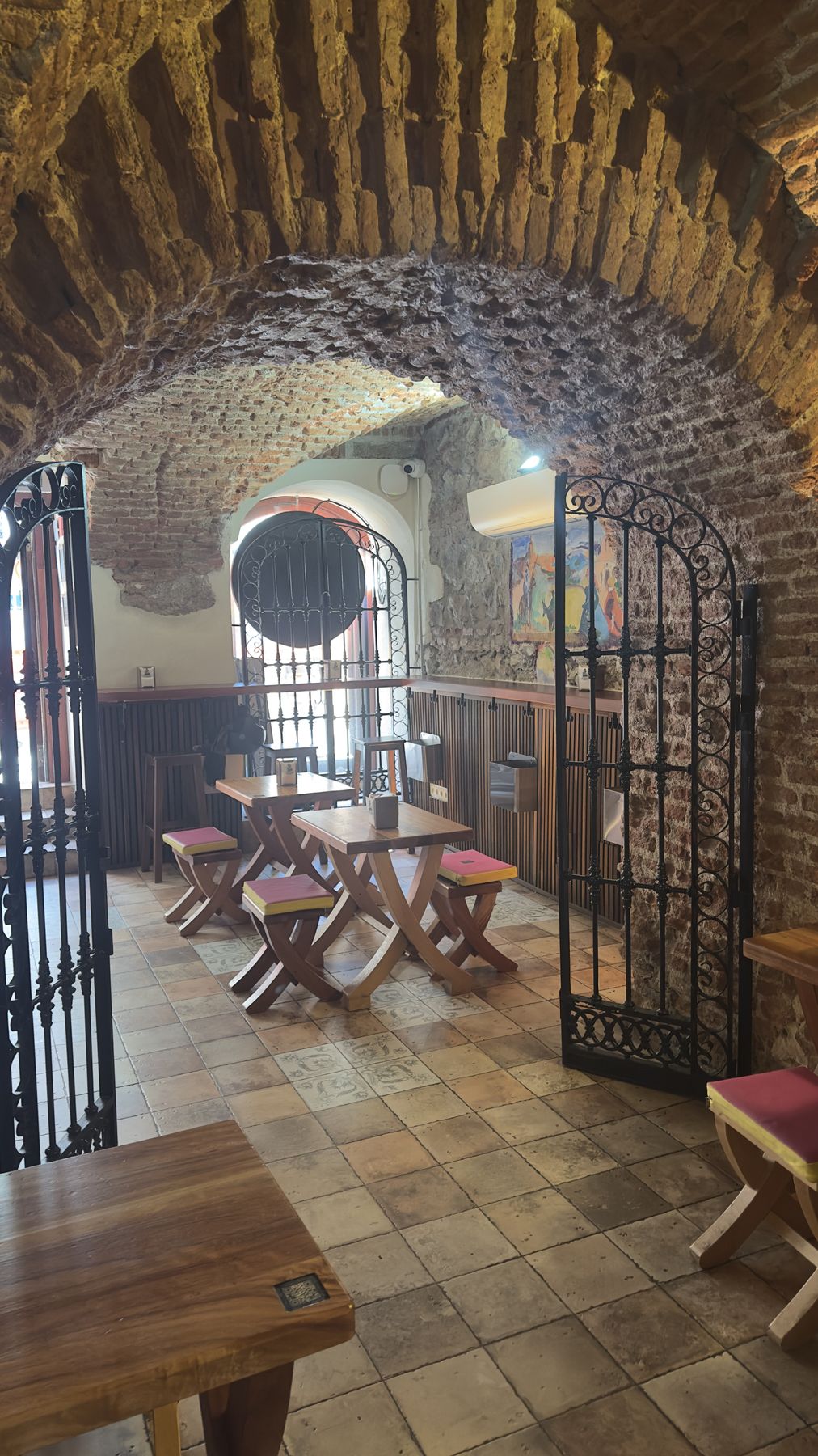 Brick-vaulted room with a wrought-iron gate and wooden tables