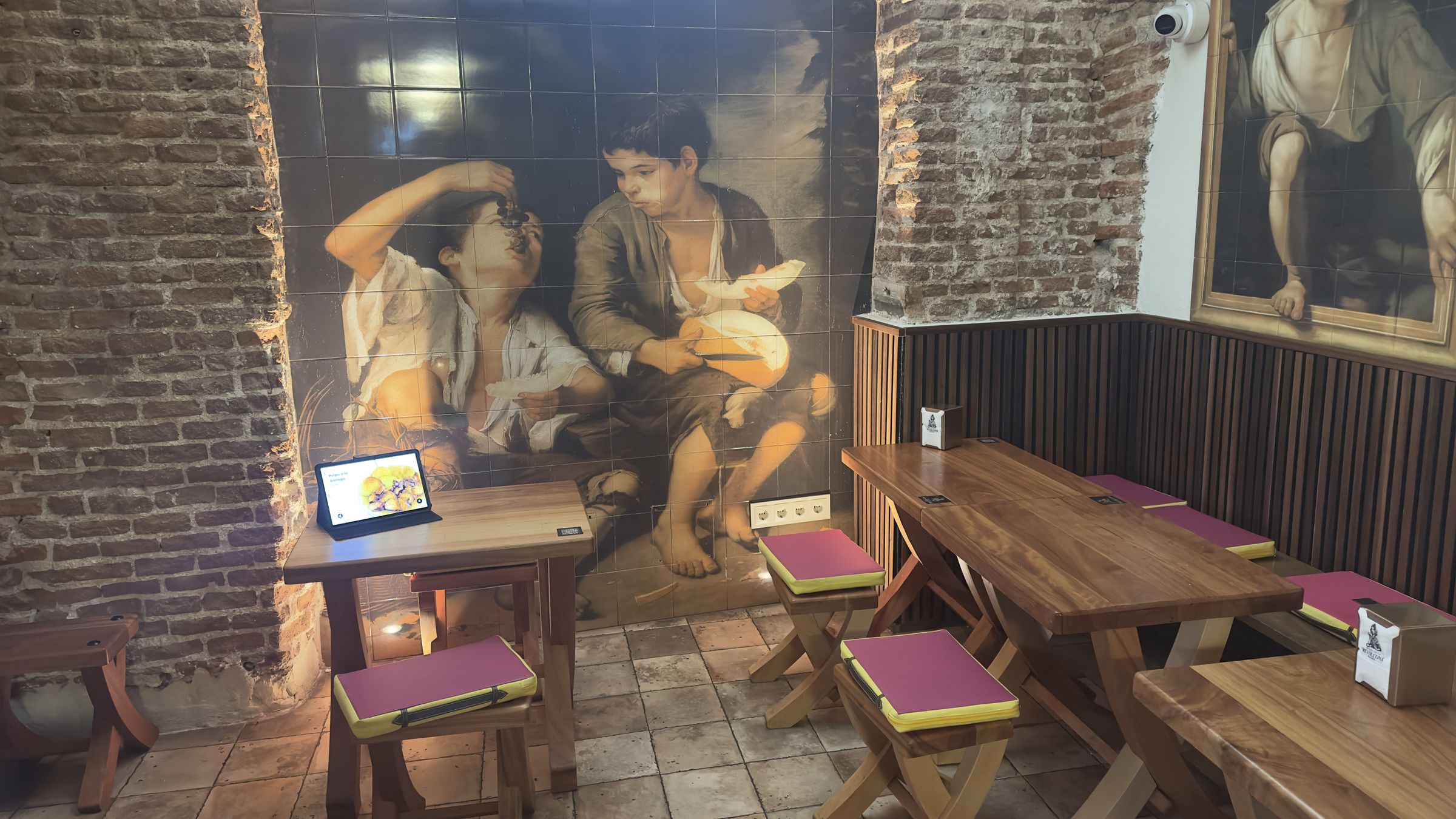 The dining room: wooden tables, brick walls and a large mural of two boys eating